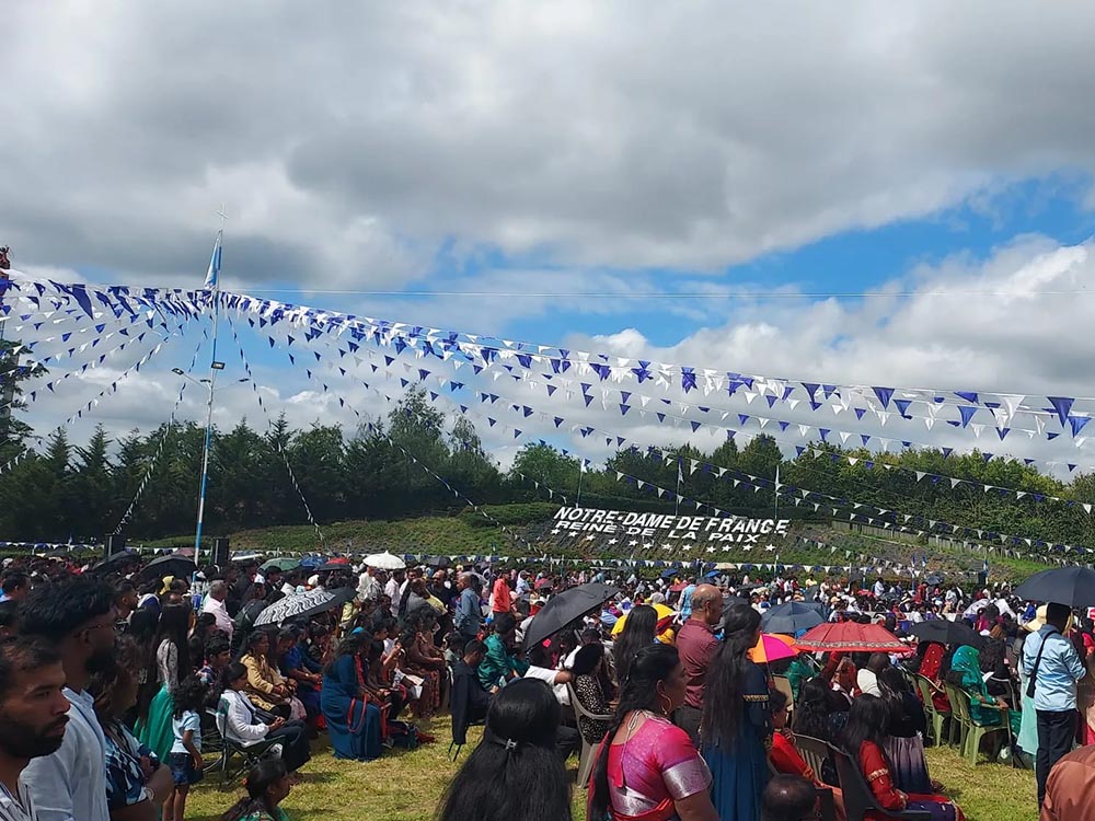 Foule de pèlerins sous les guirlandes de fanions bleus et blancs devant l'inscription Notre-Dame de France