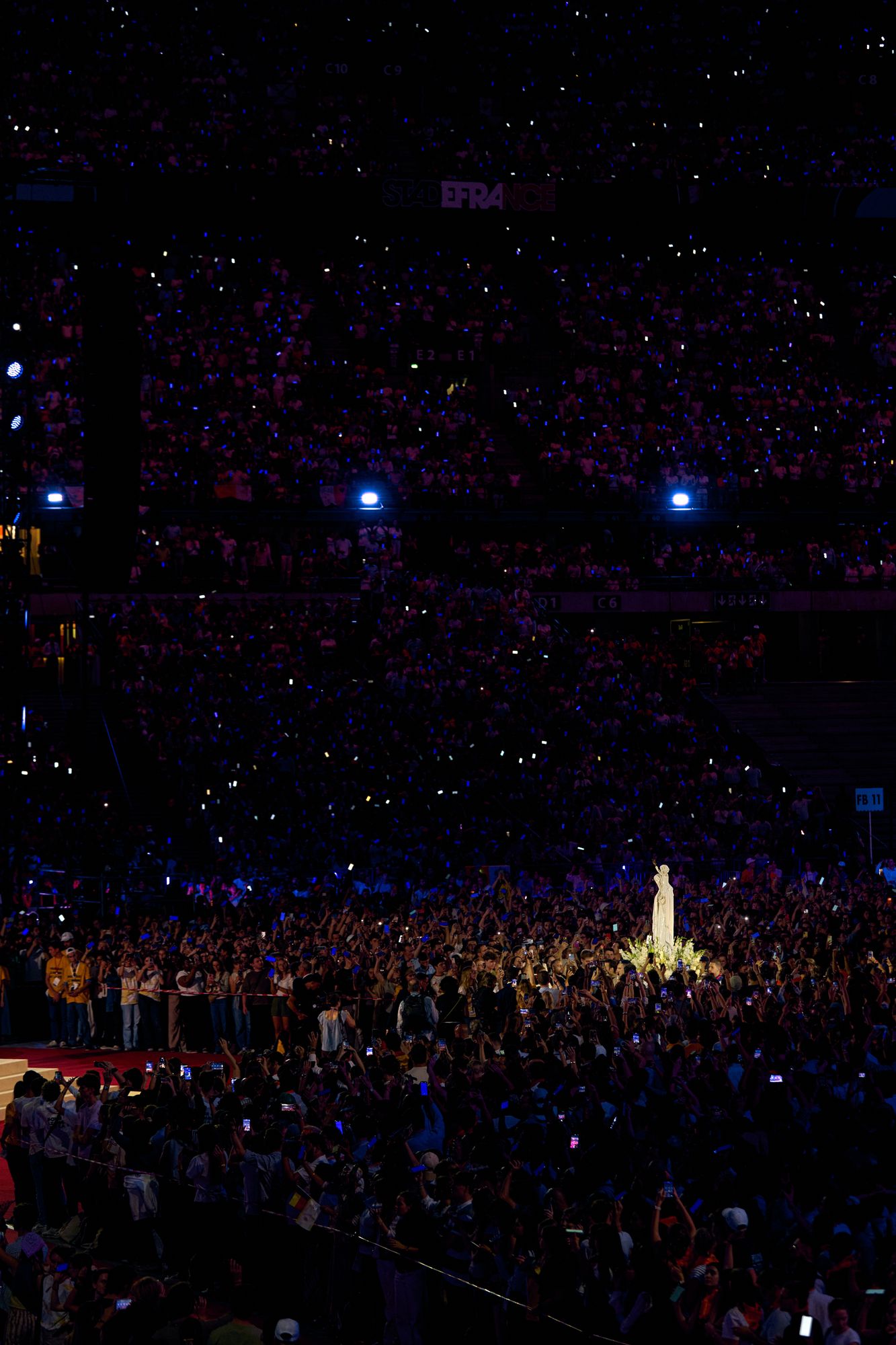 Le Stade de France dans la nuit, constellé de lumières, avec la statue de Notre-Dame de France au milieu de la foule