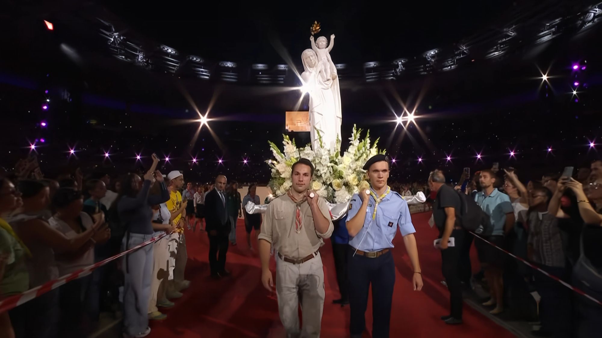 Deux scouts en uniforme portent sur leurs épaules la statue de Notre-Dame de France sur le tapis rouge du Stade de France