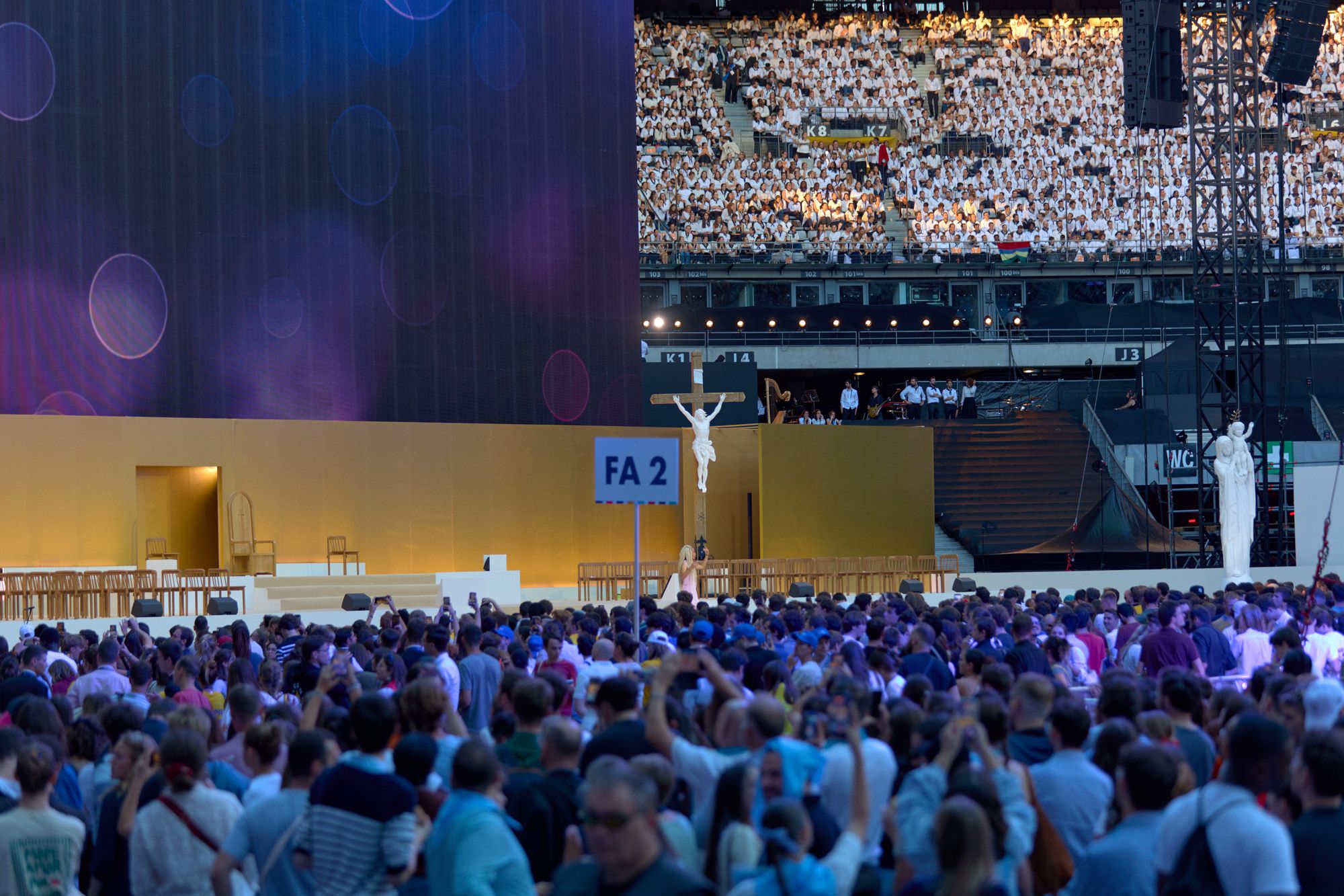 La foule des jeunes et les tribunes vêtues de blanc au Stade de France, avec la croix et la statue de Notre-Dame de France