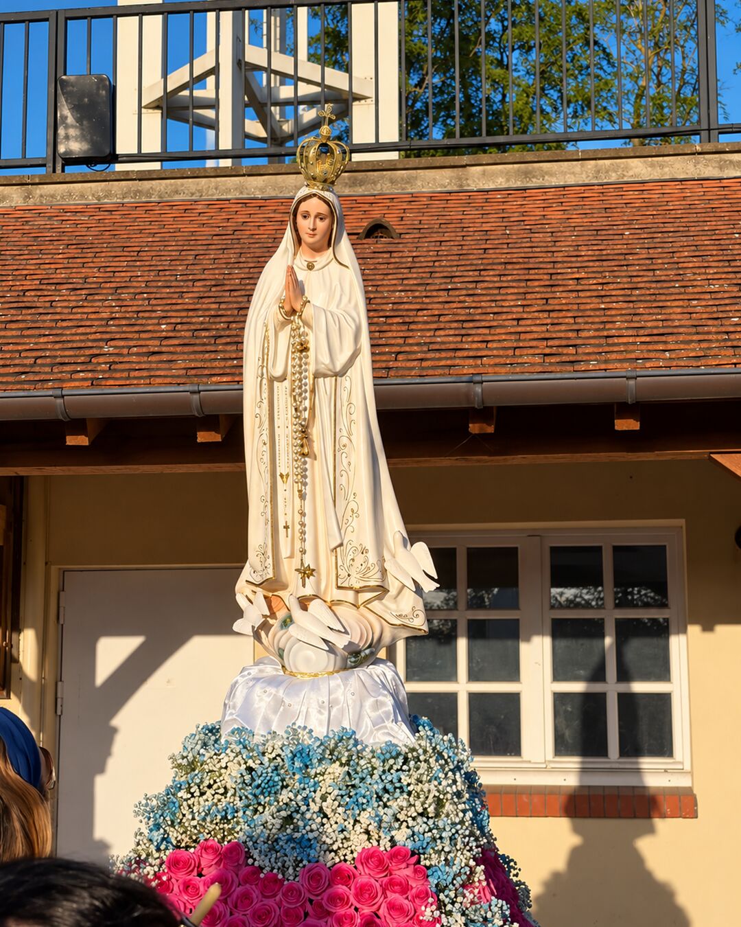 Statue de Notre-Dame de Fatima couronnée, parée de roses et de fleurs bleues