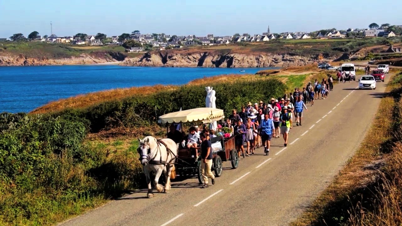 La calèche portant la statue pèlerine de Notre-Dame de France, suivie de pèlerins sur une route du bord de mer