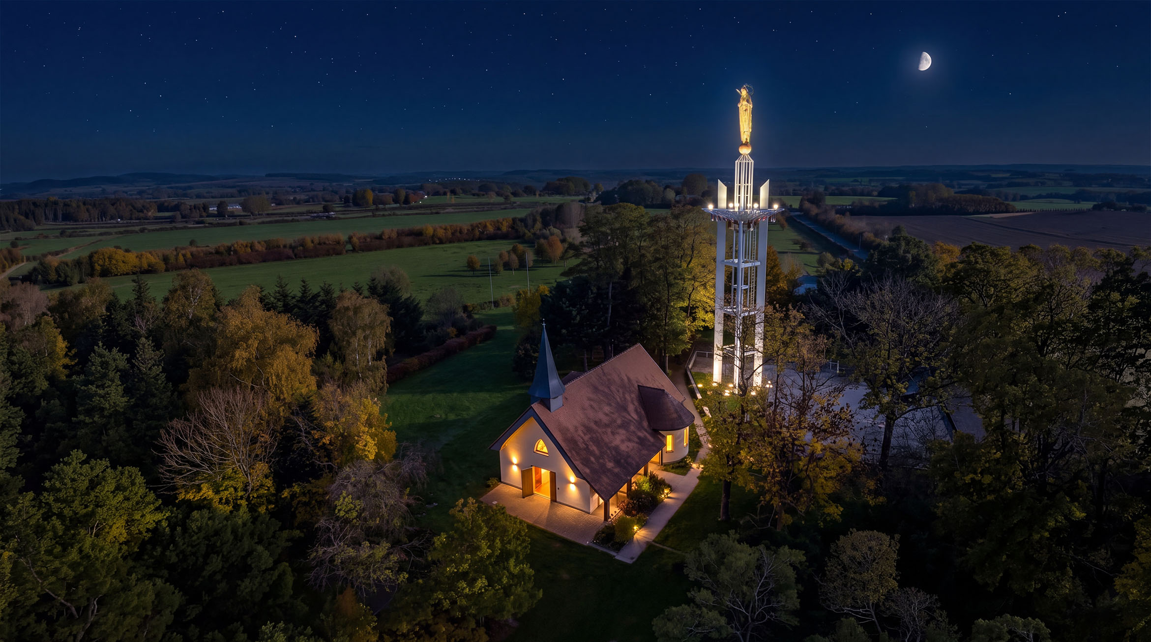 Vue aérienne de nuit du sanctuaire Notre-Dame de France à Baillet-en-France : la statue illuminée, la chapelle et la plaine de France